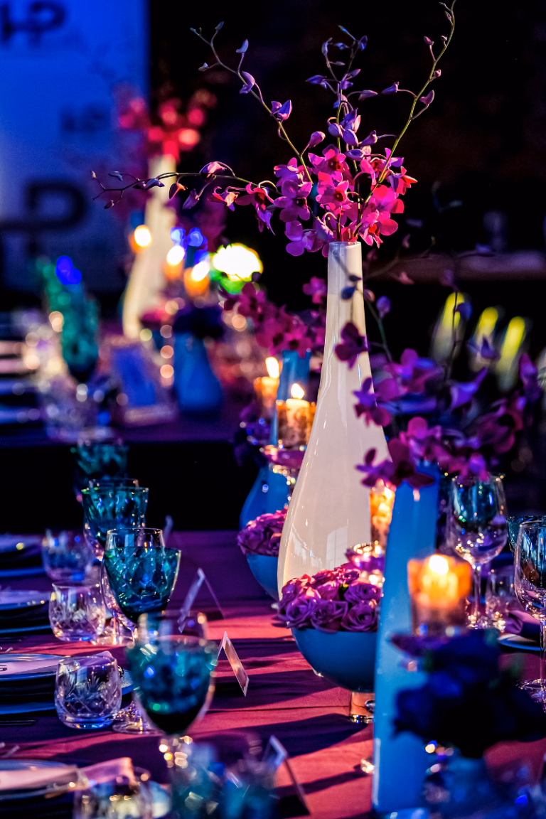 Beautiful table at a nonprofit gala or business marketing event decorated with colors of black, teal and purple. White vases sit in the center of the table holding magenta orchids.