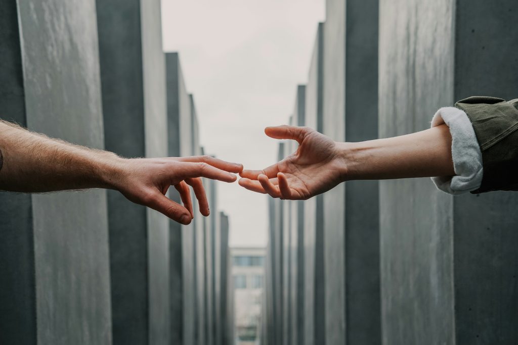 Hands reaching for help between stone pillars. Photo by Toa Heftiba on Unsplash